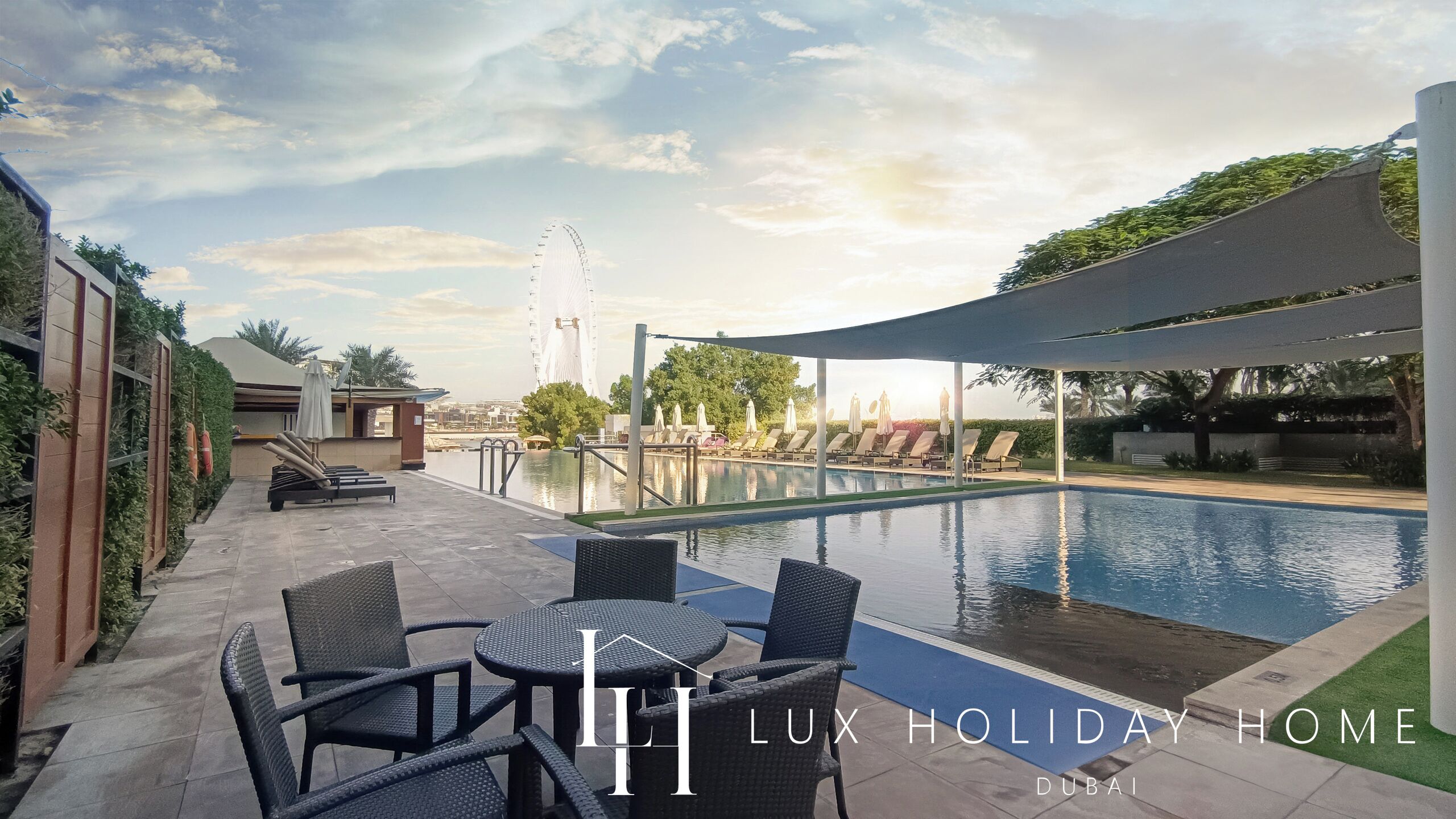 A poolside area with lounge chairs and a table, a Ferris wheel in the background, and a clear sky.