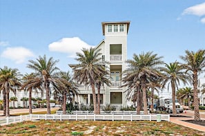 Un hotel de varios pisos con una torre central, rodeado de palmeras y una cerca blanca.