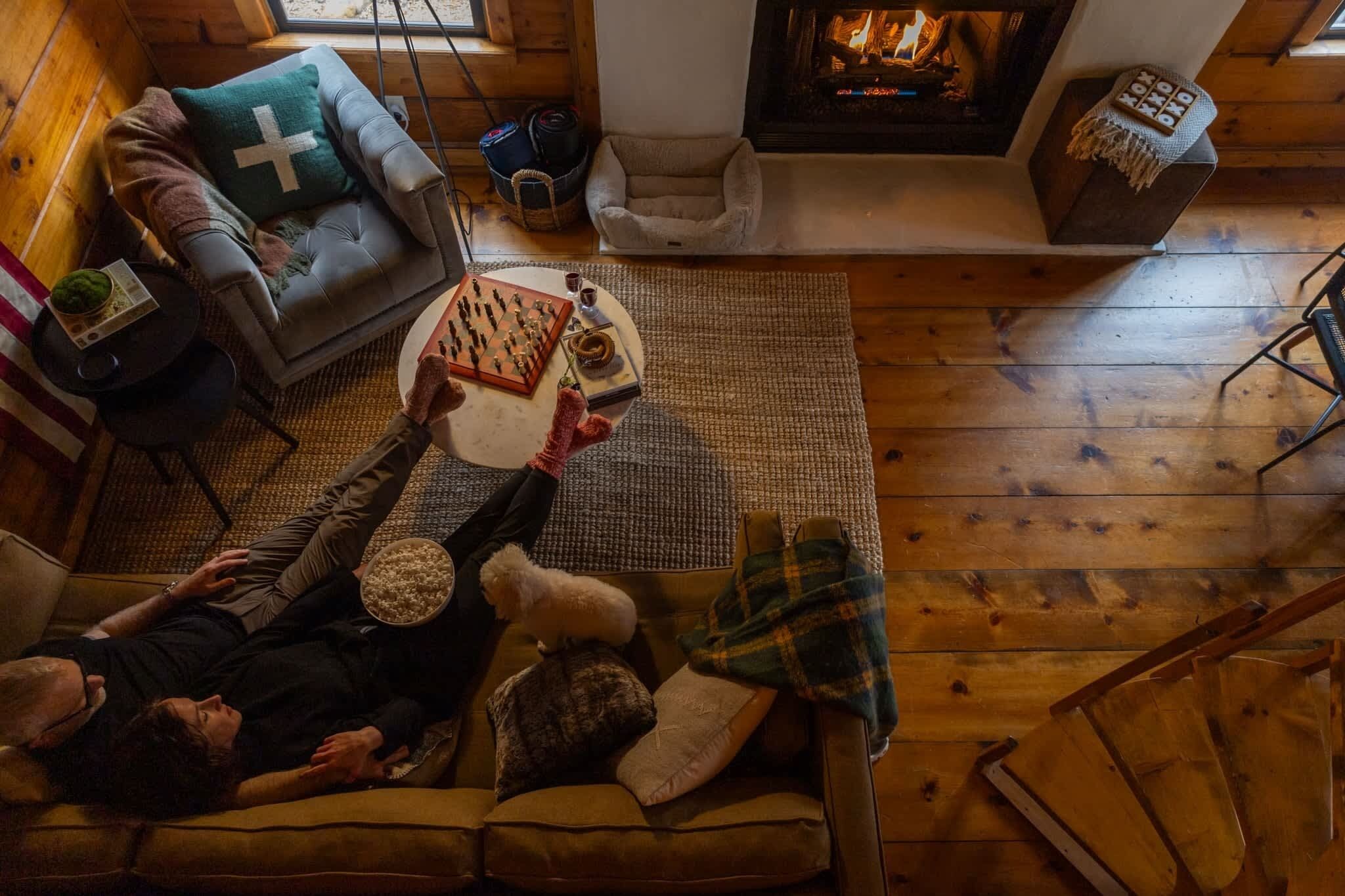A cozy living room with a fireplace, a sofa, a chair, and a coffee table with a chessboard.