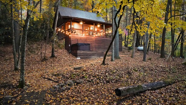 A cabin with a porch, surrounded by trees and covered in autumn leaves.