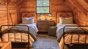 A cozy attic bedroom with two metal bunk beds, a small window, and a ceiling fan.