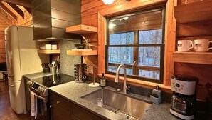 A kitchen with a stainless steel sink, a stove, and a coffee maker.