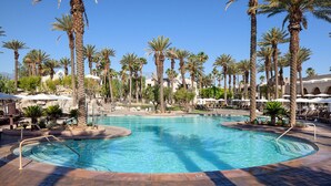 Un área de piscina con palmeras, sillas de descanso y sombrillas.