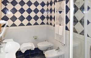 Een badkamer met een zwart-wit betegelde muur in ruitmotief, een wit wastafelmeubel, een toilet, een douchecabine met glazen wanden en een bidet.