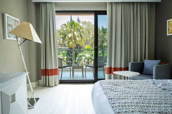 Habitación de hotel con cama, escritorio, silla, mesa y balcón con vista a palmeras.