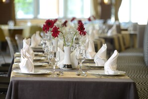 Mesa de comedor decorada con servilletas blancas, cubiertos y flores rojas en un jarrón blanco.