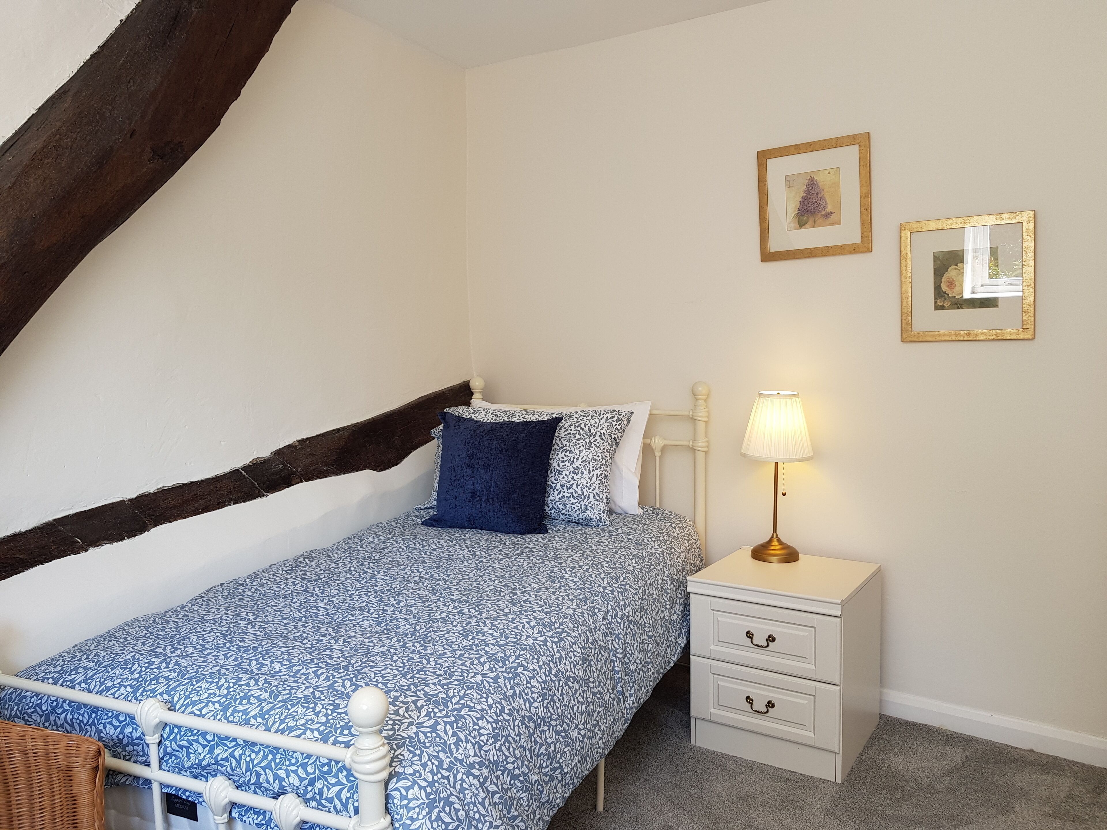 Een slaapkamer met een bed, een nachtkastje, een lamp en twee ingelijste foto’s aan de muur.
