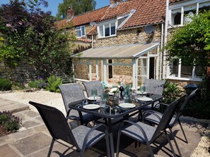 An outdoor dining area with a stone house, a covered patio, and a garden. - Cruck Cottage (Pickering)