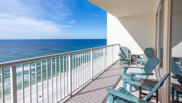 A balcony with a view of the ocean, featuring a railing, several chairs, and a table.