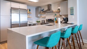 A modern kitchen with a large island, stainless steel appliances, and teal bar stools.