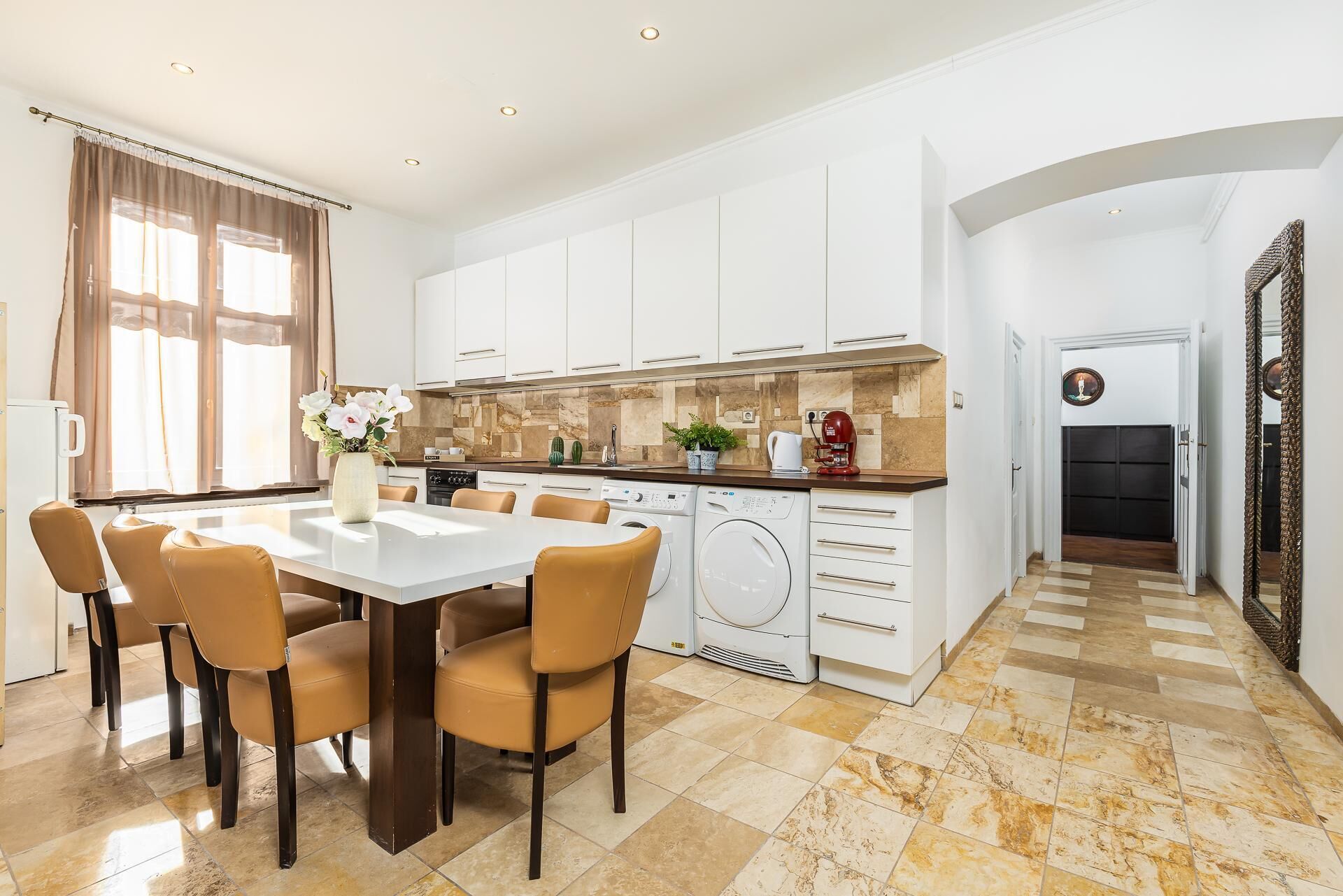 A modern kitchen with white cabinets, a dining area with a table and chairs, and a washing machine.