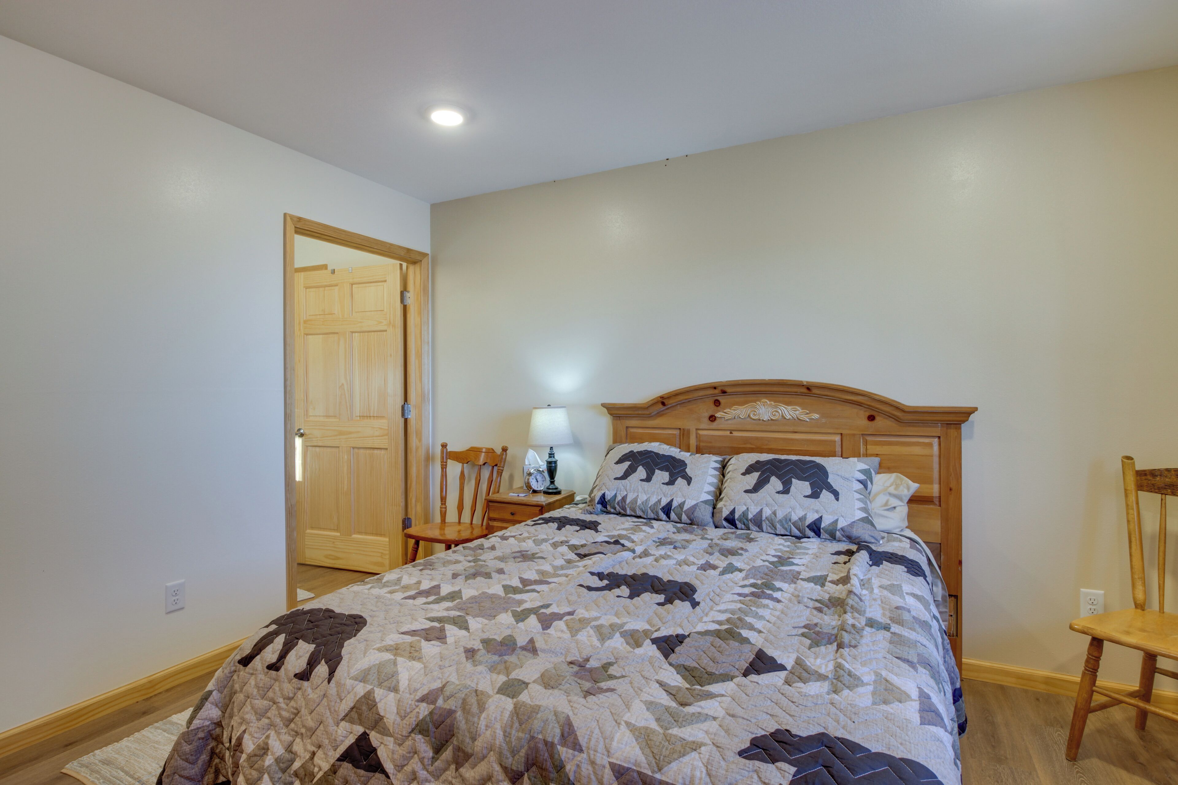 Un dormitorio con una cama de madera, una mesita de noche con lámpara, una silla y una puerta.
