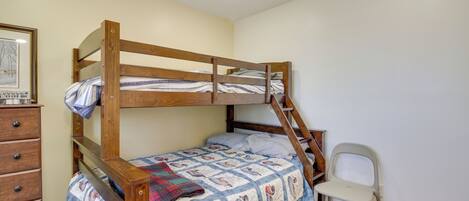 A bunk bed with a wooden frame, a dresser with drawers, a chair, and a framed picture on the wall.