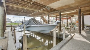 A boat docked under a wooden structure with a concrete floor, surrounded by wooden posts and a rope barrier. - Private Dock, Lanai: Bayou Retreat in Barataria! (Barataria)
