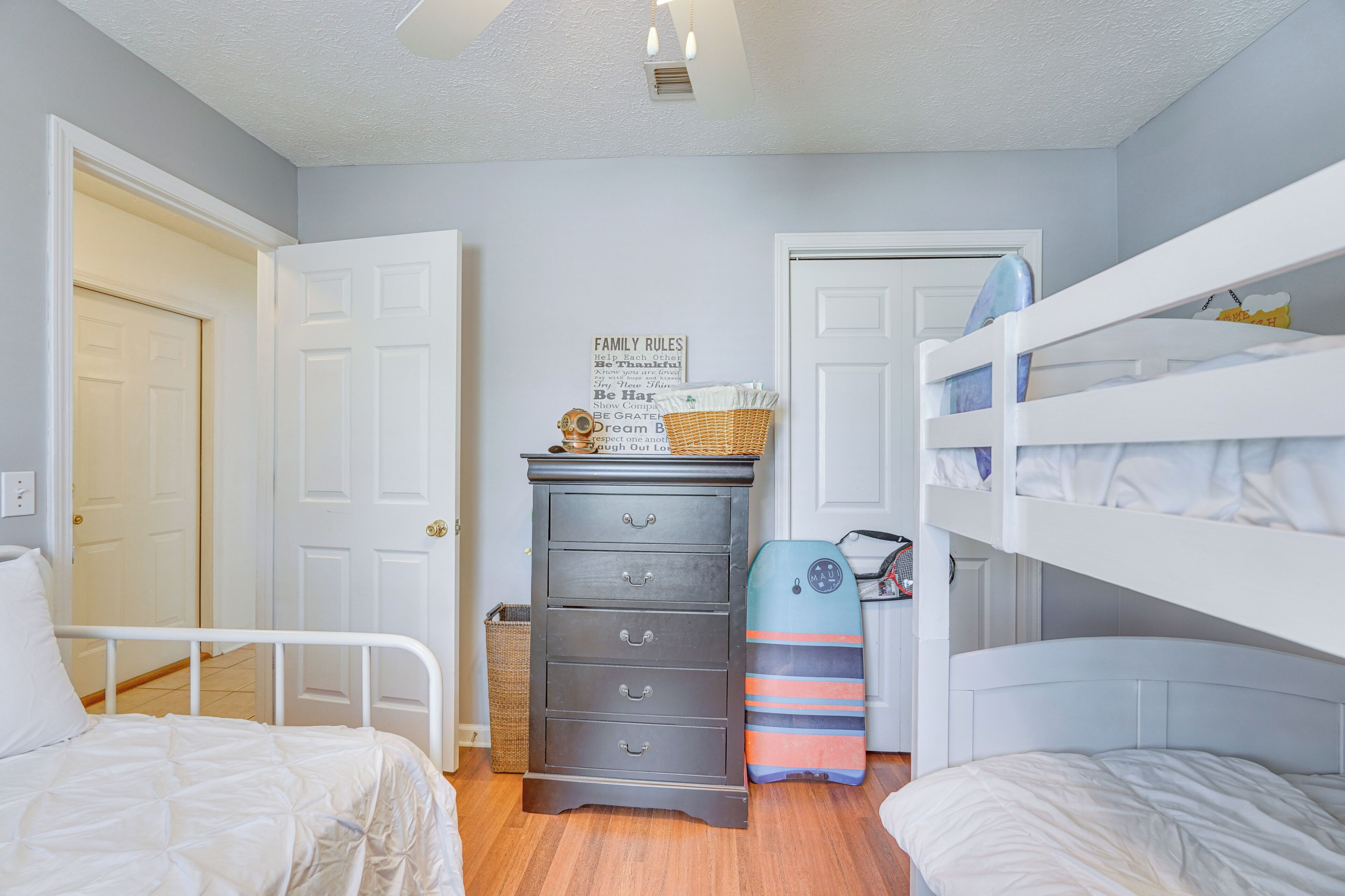 A bedroom with two beds, a dresser, and a wall-mounted shelf with a family rules sign.