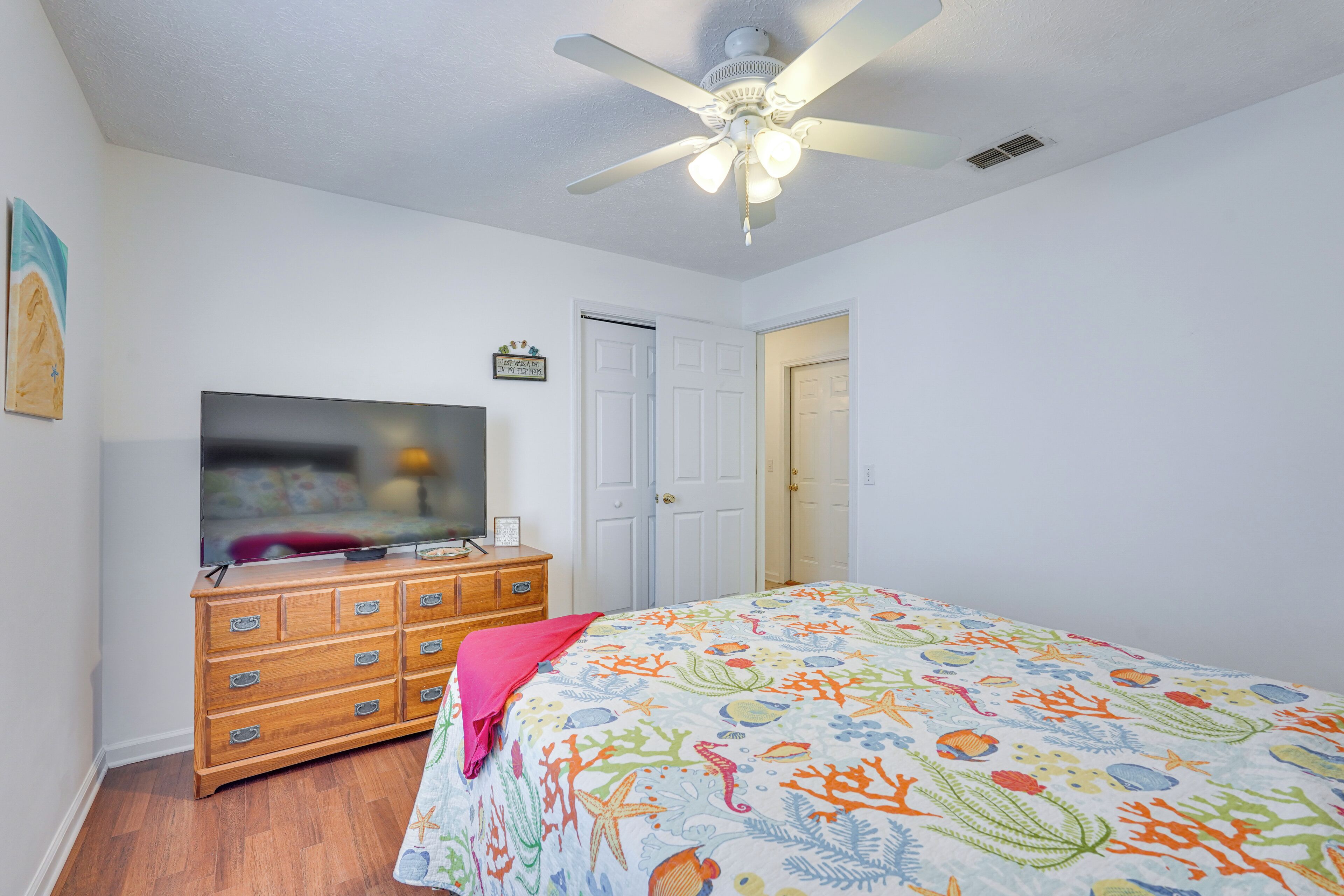 A bedroom with a bed, a dresser, a television, a ceiling fan, and a door.