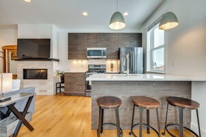 Una cocina moderna con una isla central, taburetes de bar, un microondas, un refrigerador y un televisor de pantalla plana.
