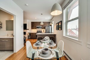 Una cocina moderna con comedor, que incluye una mesa de vidrio, platos grises y un amplio ventanal con vista a la ciudad.
