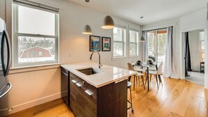A modern kitchen with a central island, large windows, and a dining area. - 2 Mi to Rmnp: Mtn-view Grand Lake Loft! (Grand Lake)