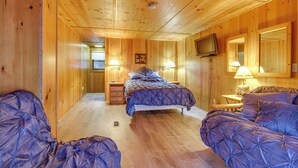 A wooden cabin room with a bed, two bedside tables with lamps, a television, and a mirror on the wall.