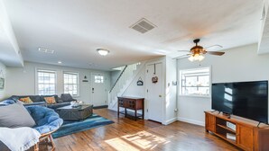 A spacious living room with hardwood floors, a large flat-screen TV, a sofa, and a staircase leading to another level. - Adorable Cottage: Fire Pit, Walk to Colonial Beach (Colonial Beach)