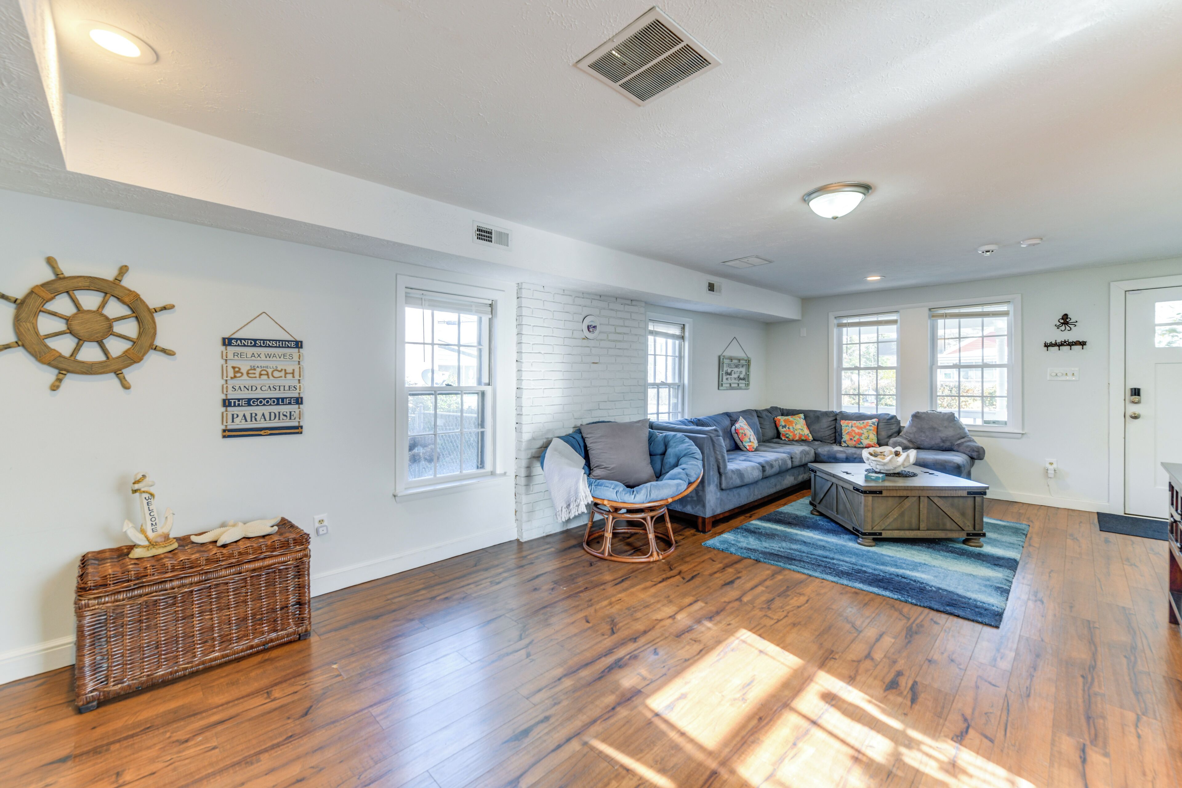 A spacious living room with hardwood floors, a blue sofa, and a wicker side table.