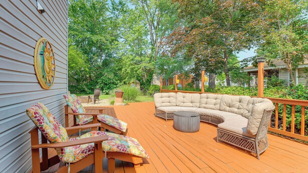 A wooden deck with a beige sectional sofa, two wooden chairs with colorful cushions, and a small round table. - Adorable Cottage: Fire Pit, Walk to Colonial Beach (Colonial Beach)