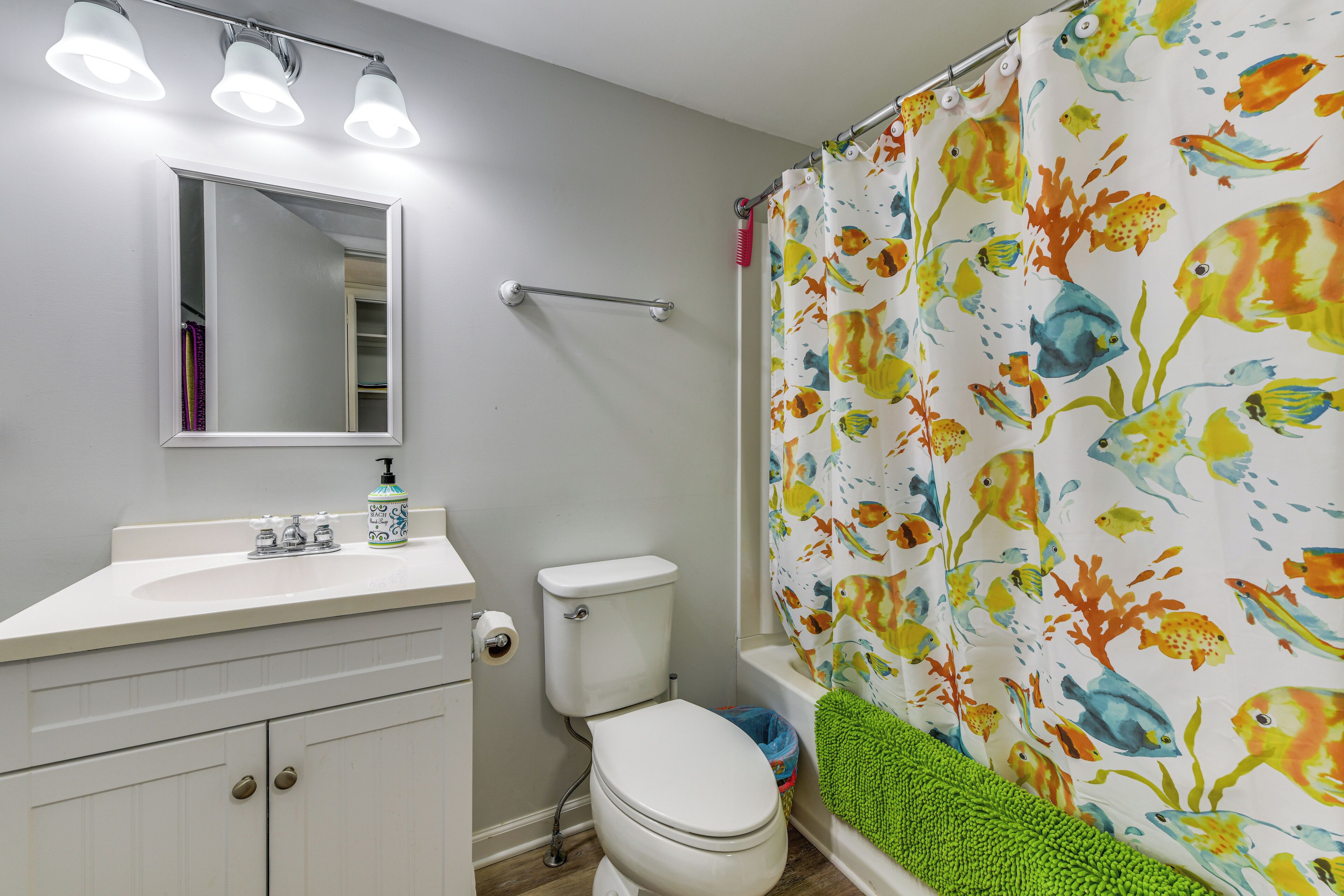 A bathroom with a white sink, mirror, and toilet. There is a shower curtain with a fish pattern.