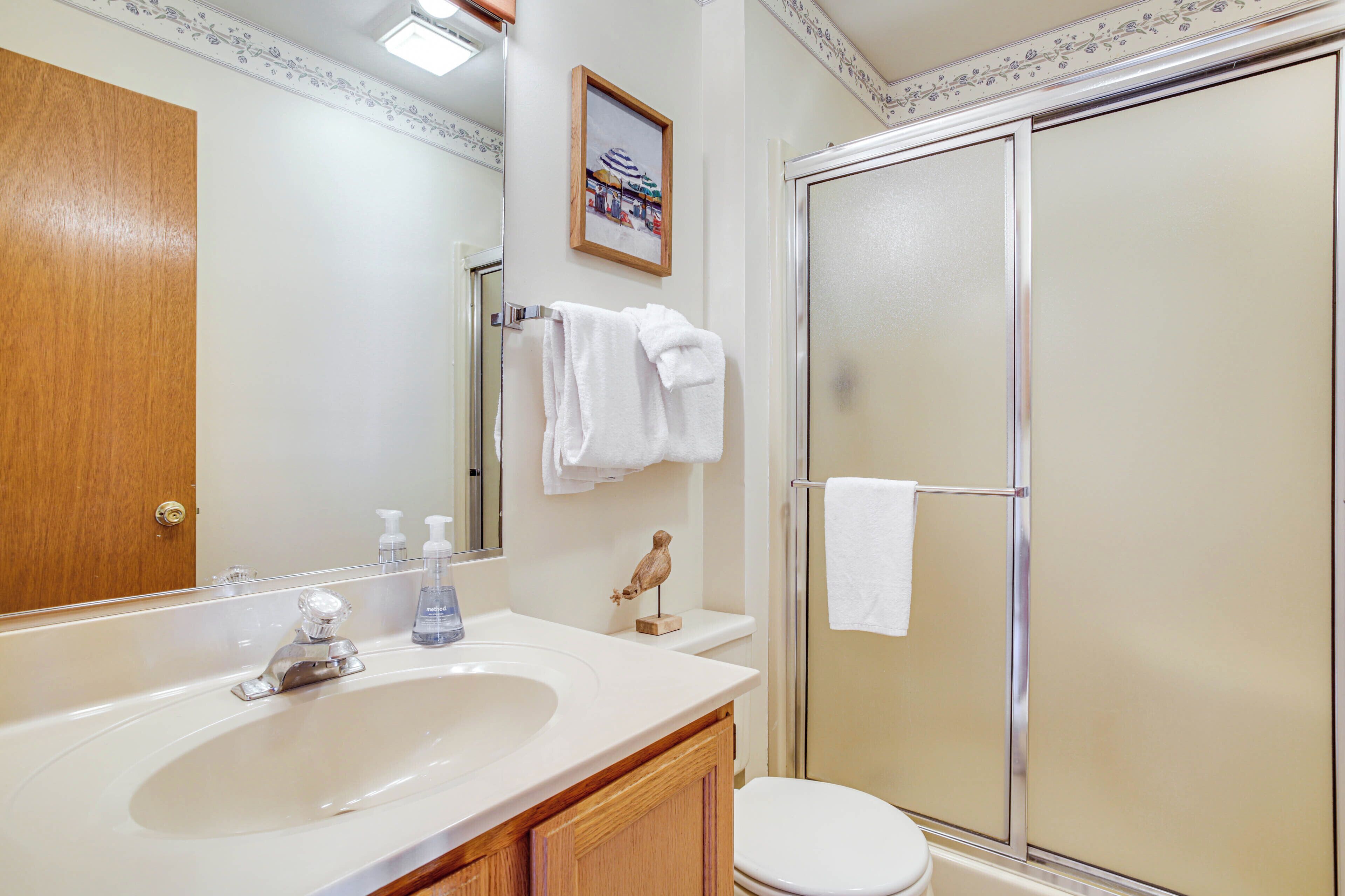 A bathroom with a sink, mirror, toilet, and shower.