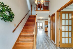 A wooden staircase leading to a second floor with a chandelier, a wooden door with glass panels, and a hallway with a wooden floor.