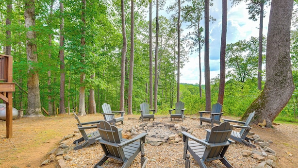 A circular seating area with Adirondack chairs around a fire pit, surrounded by a forested area.