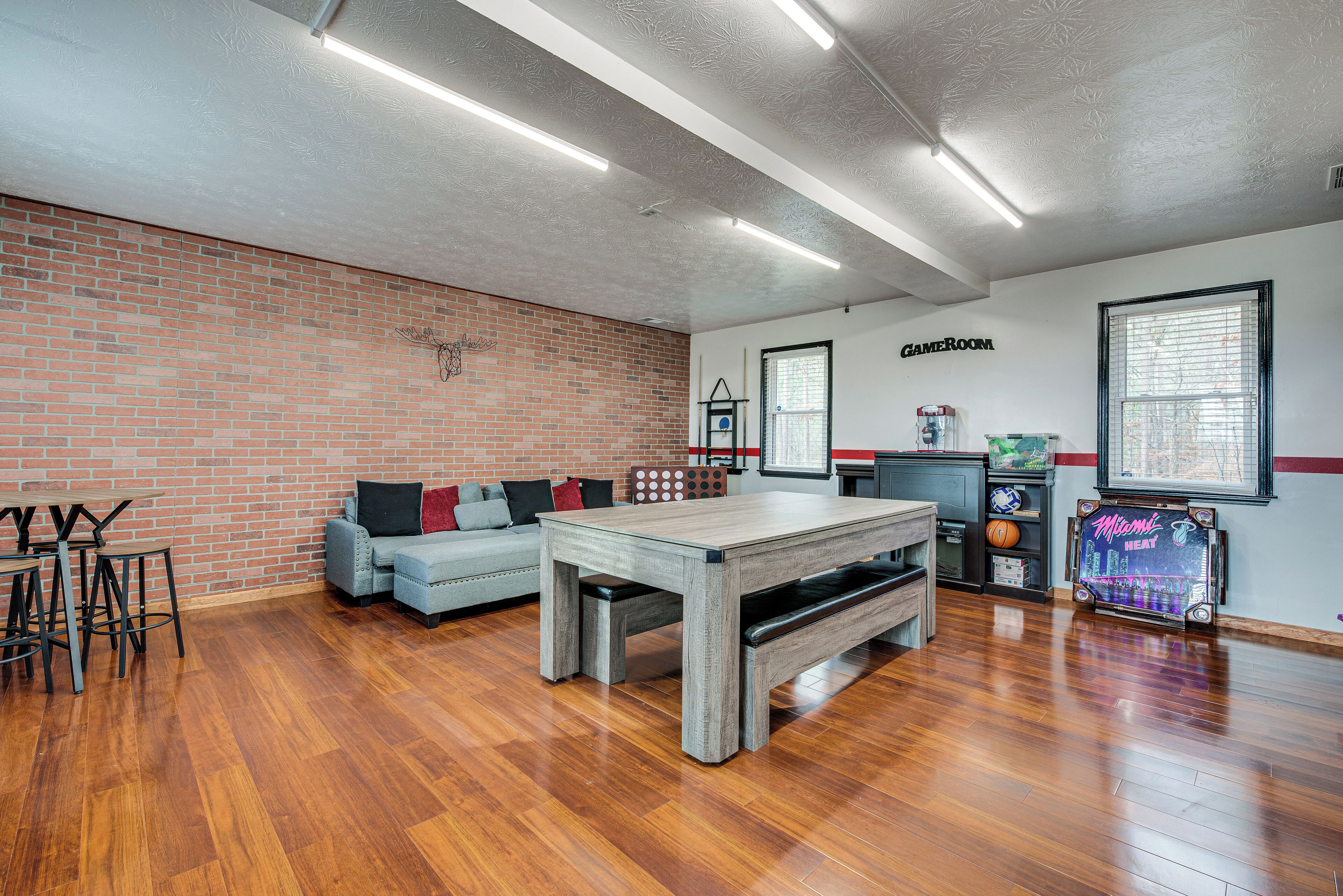 A spacious room with a wooden floor, a brick wall, a sofa with cushions, a table, and a basketball hoop.