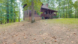 A rustic cabin with a porch, surrounded by a forest.