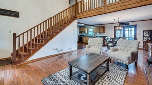 A spacious living area with a wooden staircase, a dining area, and a kitchen in the background.
