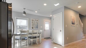 A modern kitchen with white cabinetry, a stainless steel refrigerator, and a dining area with a table and chairs.
