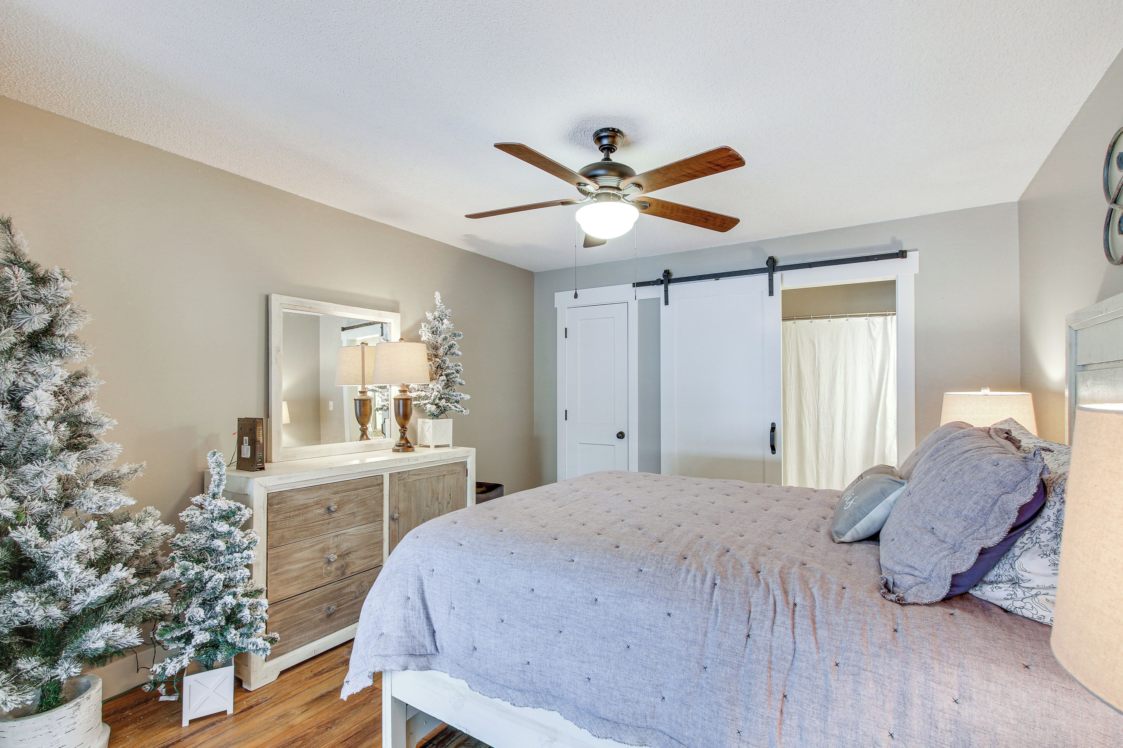 A bedroom with a bed, a ceiling fan, a dresser, a mirror, and a Christmas tree.