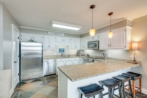 A modern kitchen with white cabinets, a stainless steel refrigerator, a granite countertop, and a bar area with stools. - Tennessee River Vacation Rental w/ Deck + View! (Counce)