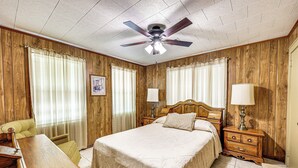 A bedroom with a wooden paneled wall, a bed with a headboard, two bedside tables with lamps, a wooden desk, and a chair.