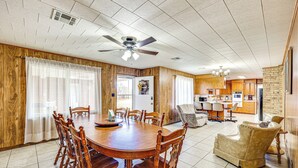 A spacious dining area with a wooden table and chairs, a ceiling fan, and a kitchen in the background.