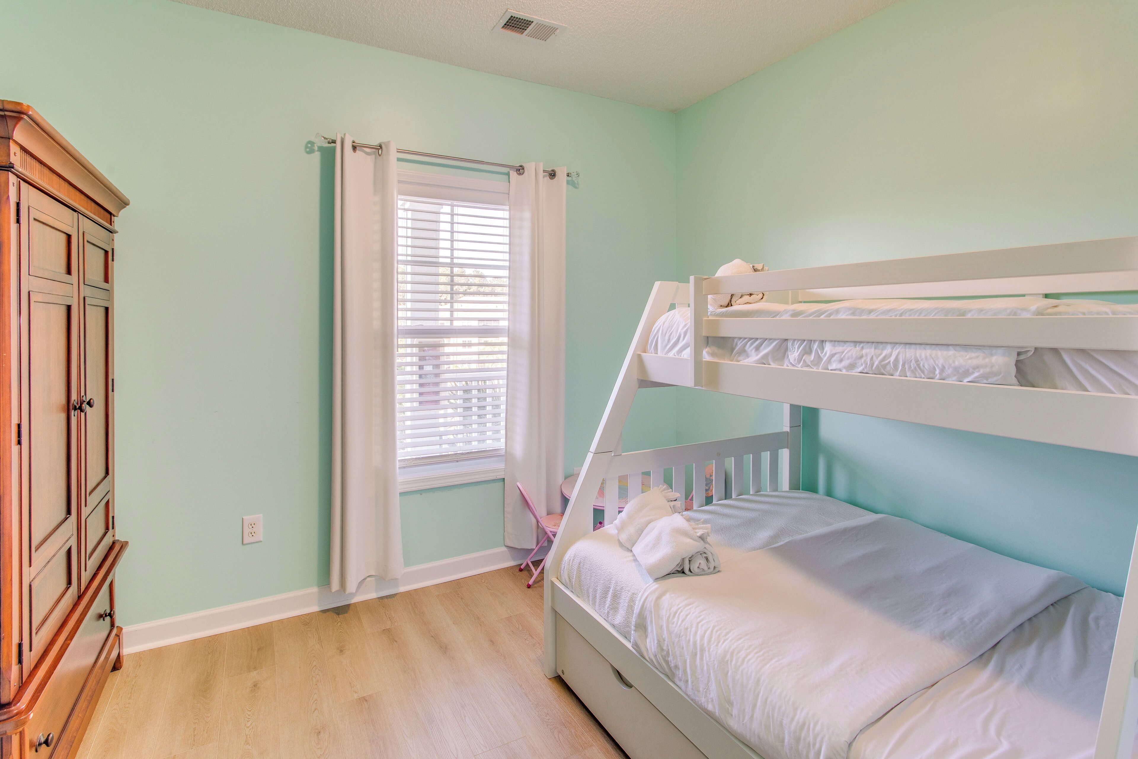 Une chambre avec un lit superposé, une armoire en bois et une fenêtre avec des rideaux.