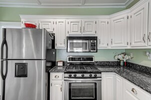 Una cocina con armarios blancos, un refrigerador de acero inoxidable, un microondas y una estufa.