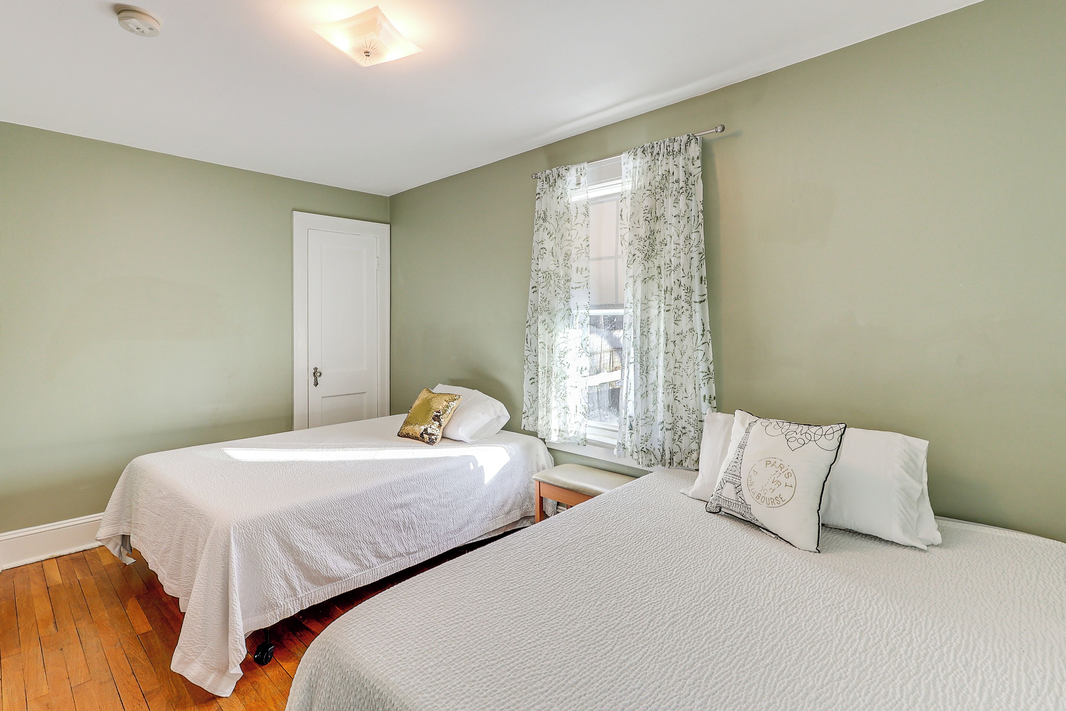 Quarto com duas camas, uma janela com cortinas florais e uma porta.