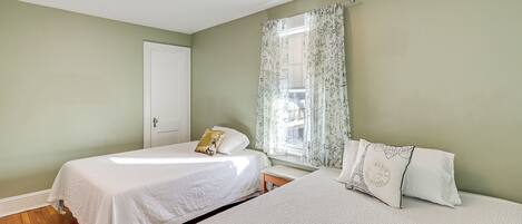 Quarto com duas camas, uma janela com cortinas florais e uma porta.