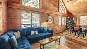 A cozy cabin interior with a sectional sofa, a dining table with chairs, and a Christmas tree. - Munds Park Cabin w/ Deck & Fire Pit: Walk to Trail (Munds Park)
