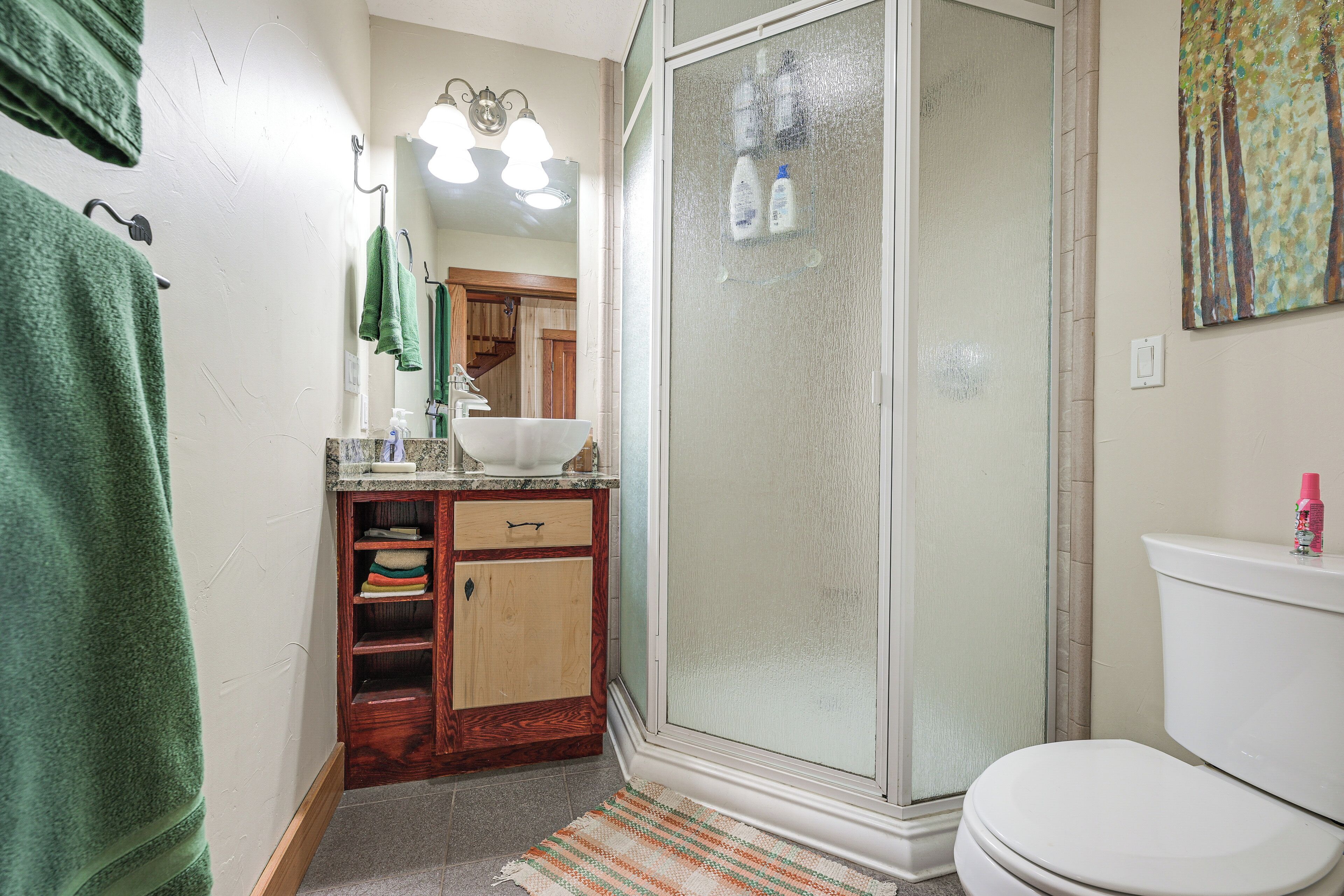 A bathroom with a shower, toilet, sink, and wooden cabinet.