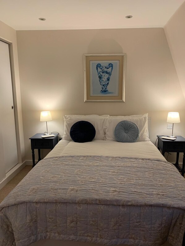 A bedroom with a bed, two bedside tables, a framed artwork, and a door.