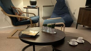 A cozy living room with two round tables, a blue armchair, a bean bag, and a fern plant. - Riding Gate Apartment (Canterbury)
