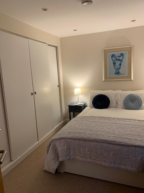 A bedroom with a bed, a nightstand, a lamp, a framed artwork, and a wardrobe.