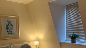 A bedroom with a bed, a bedside lamp, a window with blinds, a radiator, and a framed artwork on the wall. - Riding Gate Apartment (Canterbury)