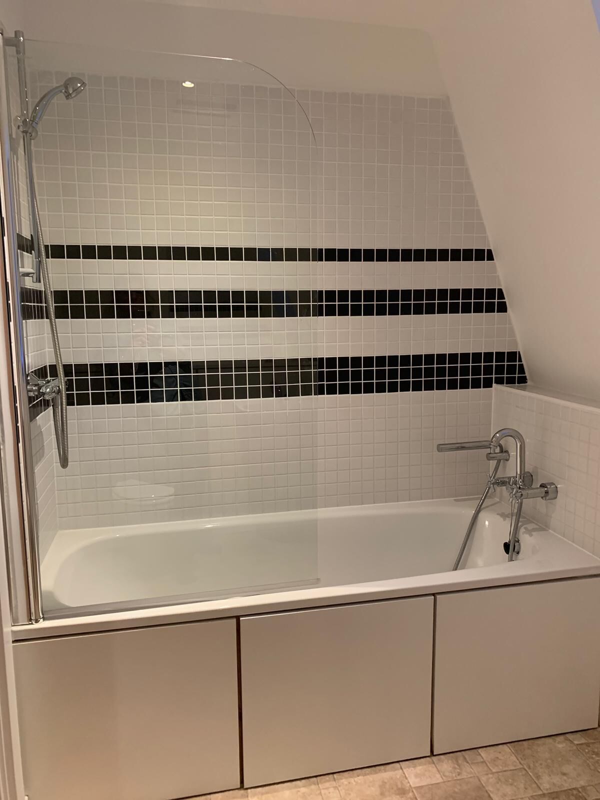 Ein modernes Badezimmer mit freistehender Badewanne, einer Duschkabine und einer Wandverkleidung mit schwarz-weißen Fliesen.